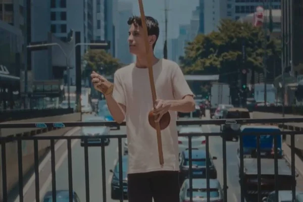 imagem colorida de homem branco com camisa branca tocando berimbau