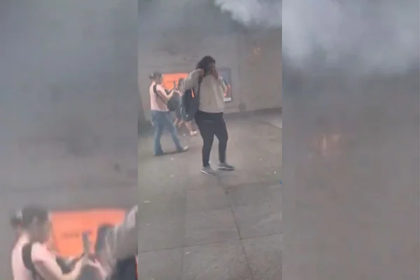 Imagens coloridas mostram uma mulher em pé, blusa clara, com o rosto coberto por um lenço, outra mulher do lado esquerdo dela, fumaça no canto alto direito da imagem