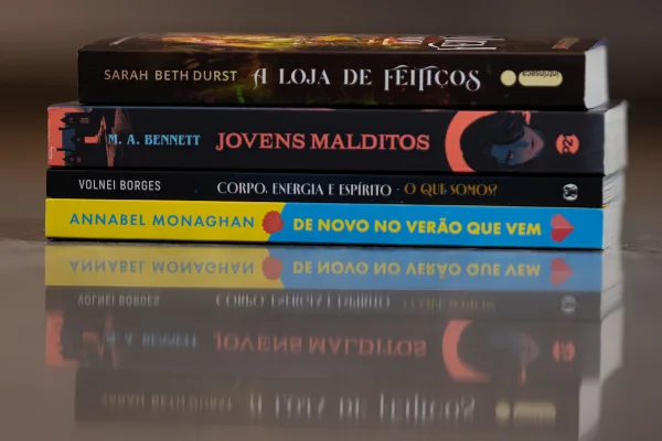 foto colorida com quatro livros deitados, um sobre o outro, formando uma pilha sobre uma mesa - metrópoles