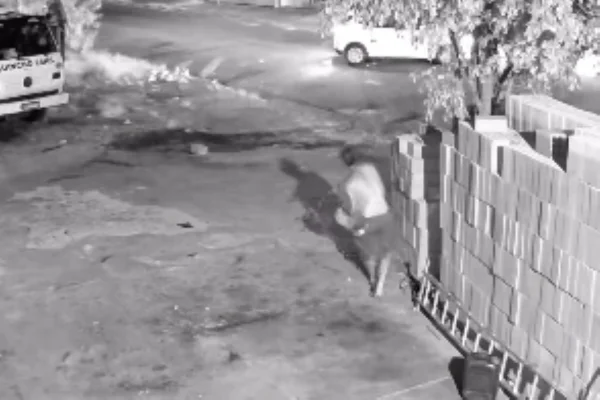 Imagem preto e branco de homem jogando tijolos em um carro. Metrópoles