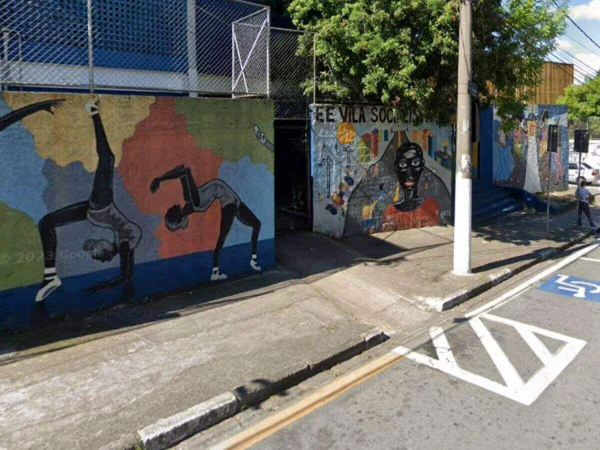 Foto colorida mostra faixada da escola Vila Socialista com muro colorido e árvores