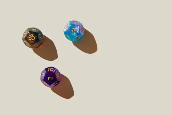 Três dados dodecaedros, de doze lados, com símbolos de cada signo em dourado espalhados em mesa branca - Metrópoles