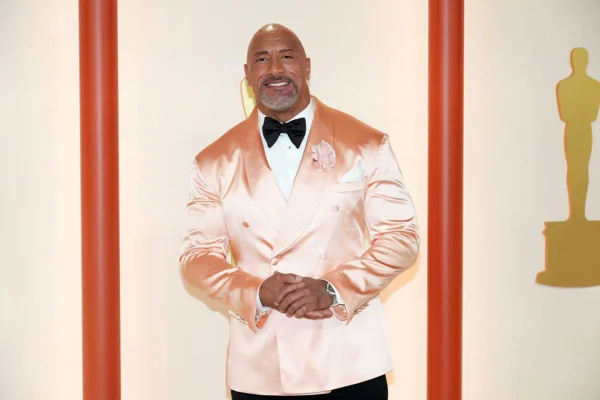 Dwayne Johnson de terno rosa claro posa sorrindo de maos dadas - metrópoles
