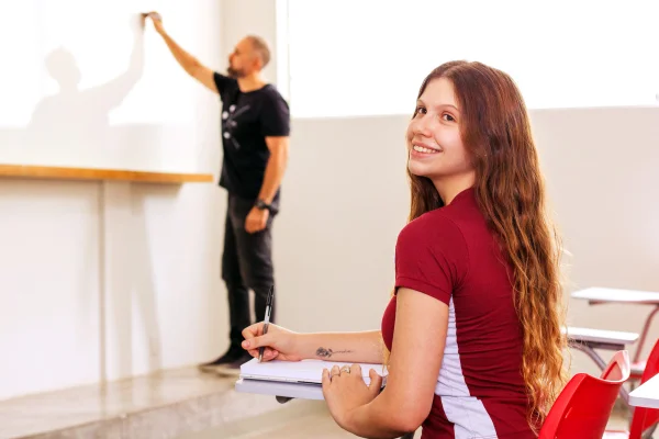Fotografia colorida mostrando aluna assistindo aula de professor em sala-Metrópoles