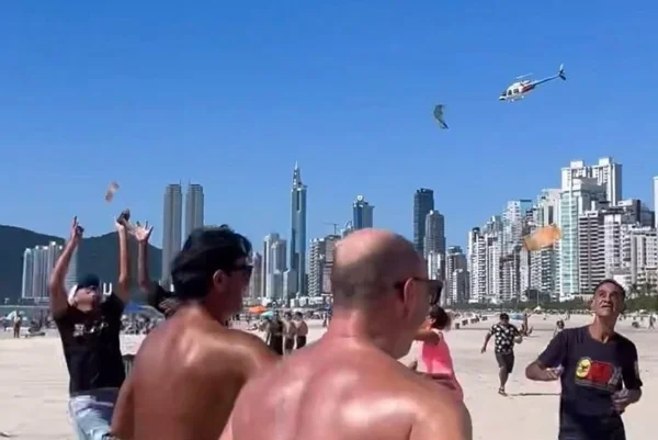 Imagem colrida de helicóptero jogando dinheiro em praia de balneário camburiú