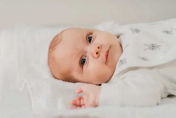 Foto de bebê deitado em cama, olhando para câmera - Metrópoles