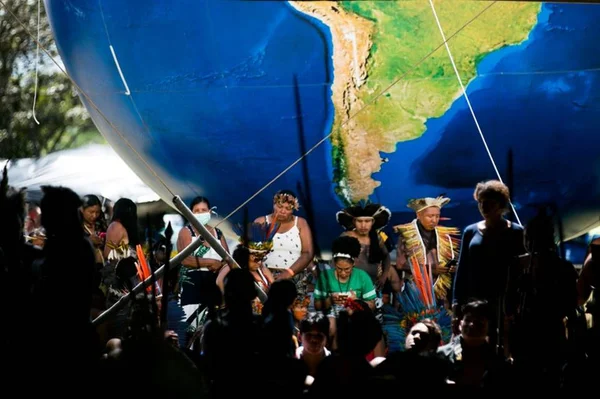 Indígenas no acampamento Terra Livre acampados no Eixo Monumental, em Brasília, reunidos num círculo e próximos de um balão inflável em forma de globo terrestre - Metrópoles