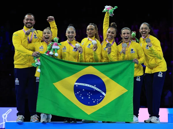 Imagem mostra time feminino de ginástica artística do Brasil posando com bandeira do Brasil- Metrópoles