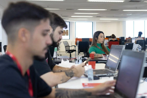 Três estagiários da segunda turma do programa de estágio Mentor mexem em computadores - Metrópoles