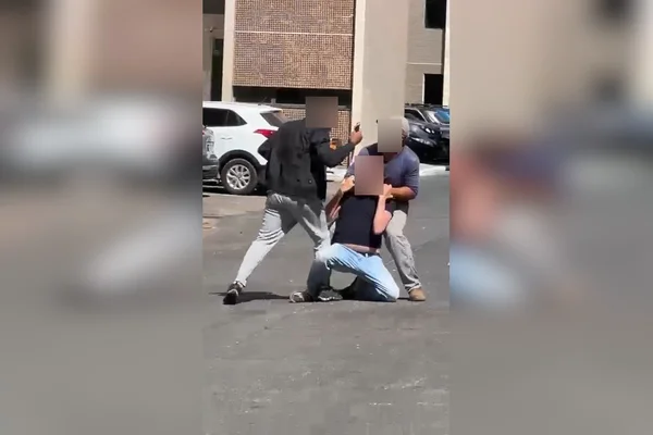 Tutor de cachorro que matou outro na Asa Sul é imobilizado e contido com faca por dois outros homens. Na foto, o alvo está ajoelhado e os outros dois o seguram e ameaçam com a faca em estacionamento - Metrópoles