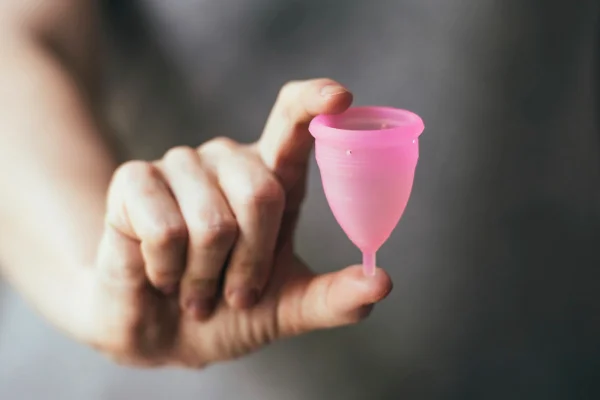 Mão segurando coletor menstrual rosa