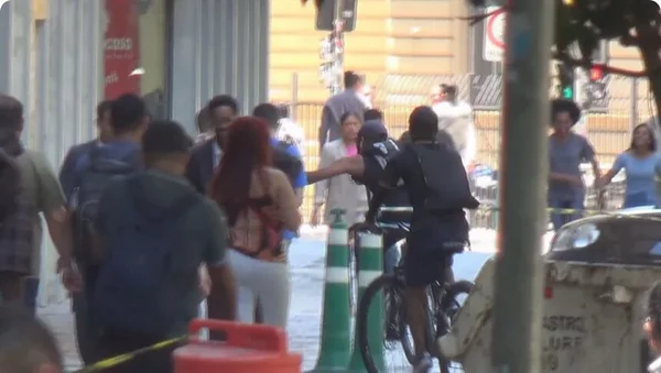 Em foto colorida criminoso em bicicleta pega celular de vítima em calçada no centro de São Paulo - Metrópoles