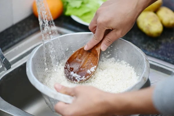 Foto em close up lavando arroz branco na pia. Metrópoles