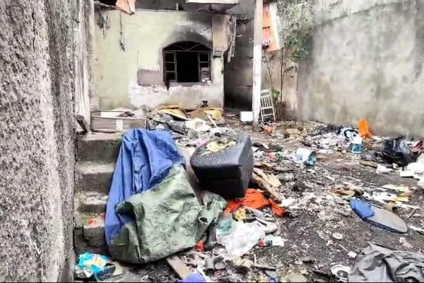 Foto colorida de entulho e sujeito em quintal, em frente à casa abandonada - Metrópoles