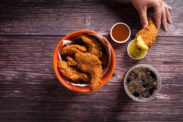Na foto, um balde de frango frito com molhos