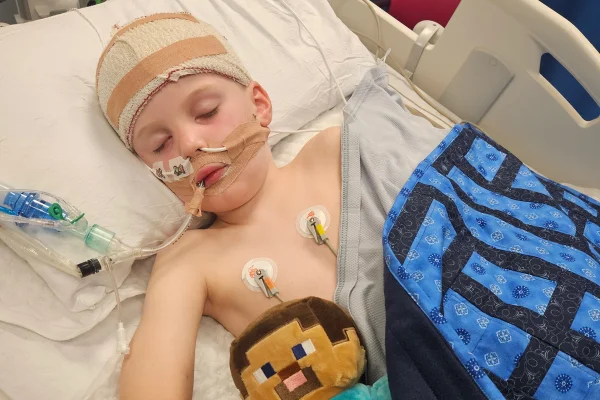 Foto colorida de criança em maca hospitalar, conectada a tubos e com a cabeça enfaixada - Metrópoles