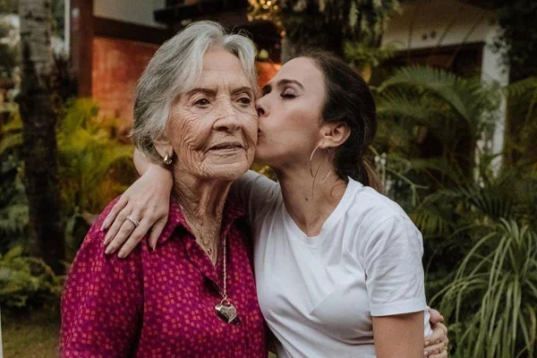 Imagem colorida de Tata Werneck e Dona Vera, sua avó. Tata beija a idosa no rosto, que sorri - Metrópoles