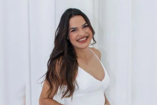 Mulher branca com cabelos ondulados e blusa branca, sorrindo - Metrópoles
