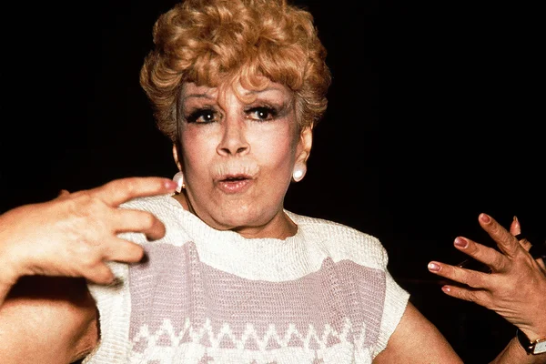 Imagem colorida de Dercy Gonçalves usando roupa branca e olhando para a câmera - Metrópoles