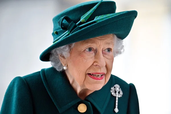 Mulher idosa com chapéu e roupas verde. Ela está de batom vermelho e com um broche de pedras preciosas