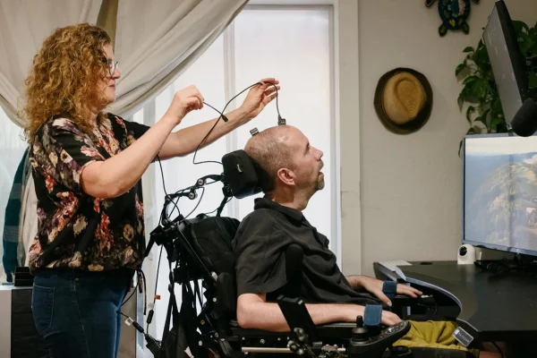 Imagem mostra uma mulher esticando fios ligados à cabeça de um homem em cadeira de rodas - Metrópoles