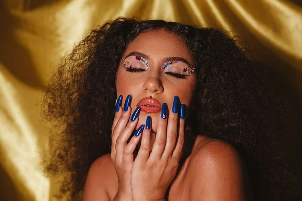 Na imagem com cor, mulher negra com os cabelos crespos posa com os olhos fechados e mãos sobre o rosto - Metrópoles