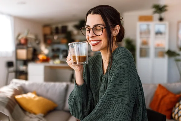 Mulher levanta xícara de café sorrindo - metrópoles