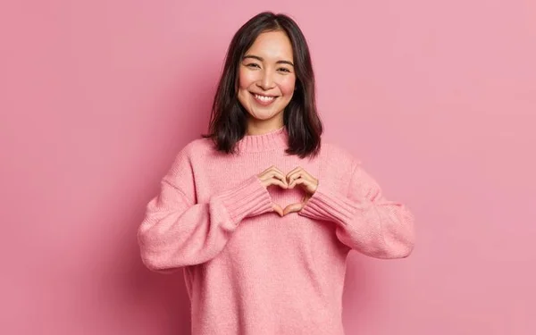 Mulher com roupa rosa fazendo um coração com as mãos