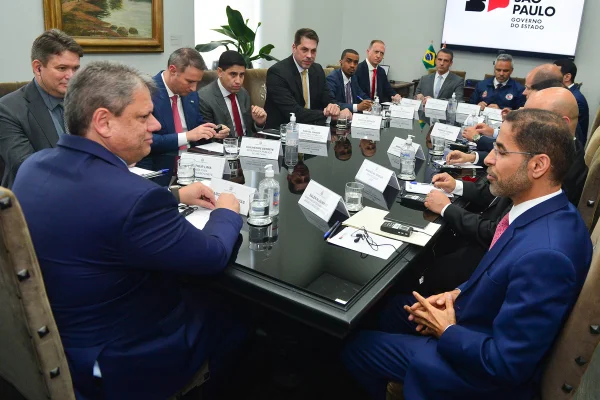 Imagem colorida mostra sala de reunião com mesa repleta de homens de roupas sociais - Metrópoles
