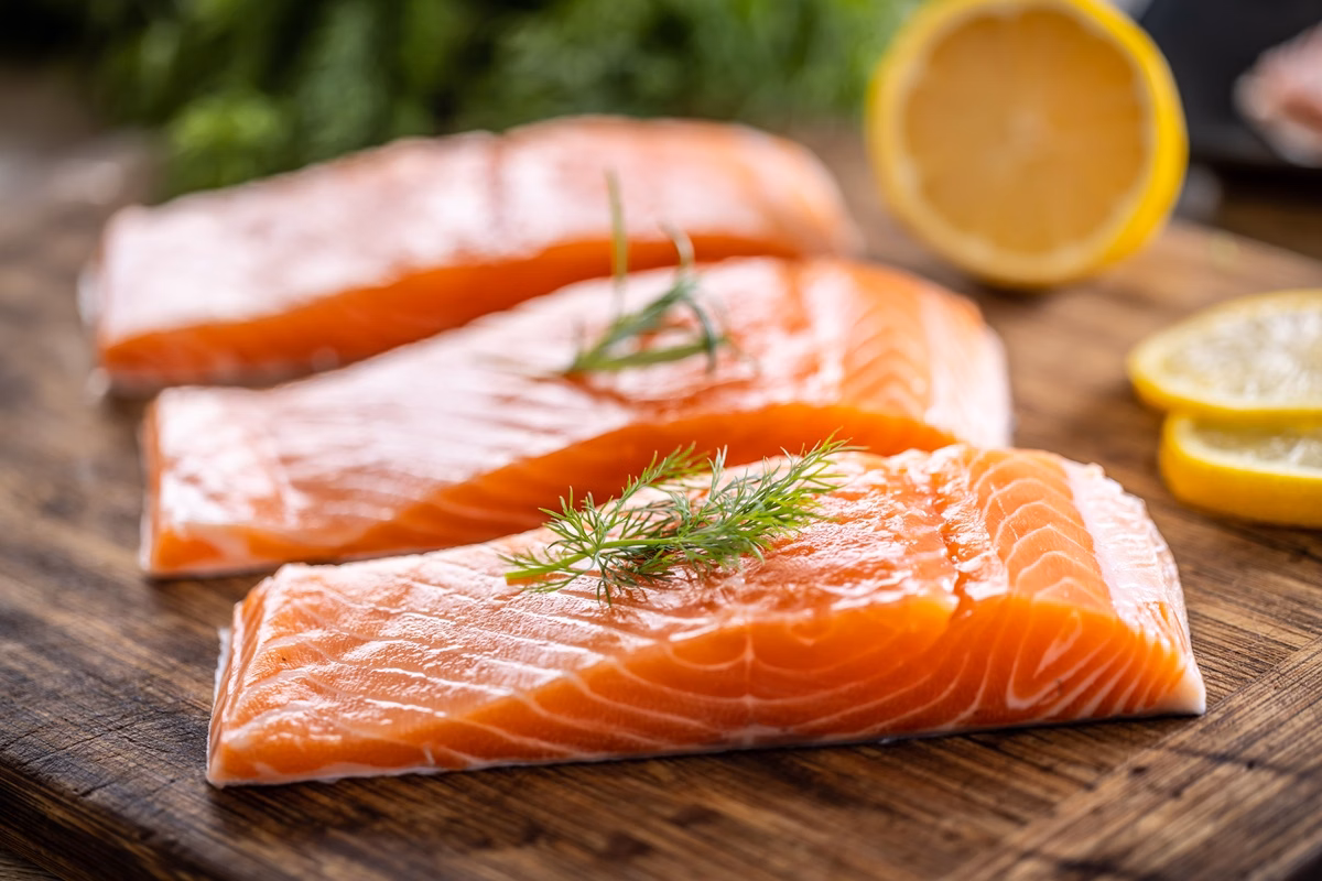 Foto de stock de Filetes de salmão cru em tábua de madeira com endro, alecrim e limão - 5 alimentos que podem fortalecer a saúde mental e o bem-estar
