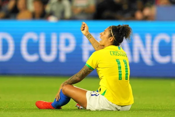 Cristiane, em foto colorida, sentada na grama, com a camisa da seleção