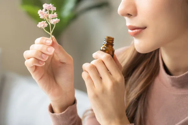 mulher cheirando um vidro com aroma de flores