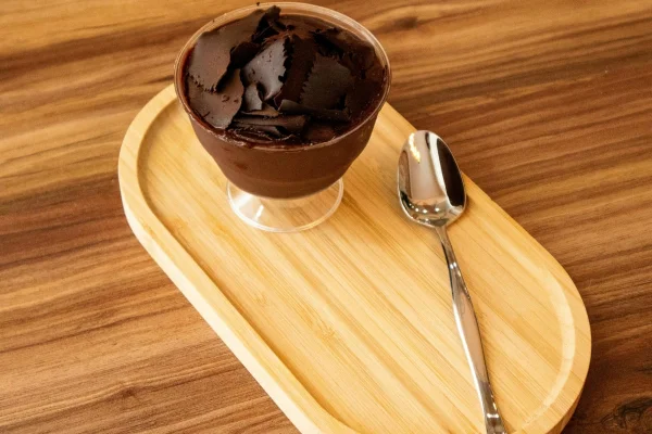 Pote com mousse de chocolate servido em uma bandeja de madeira e colher prata ao lado