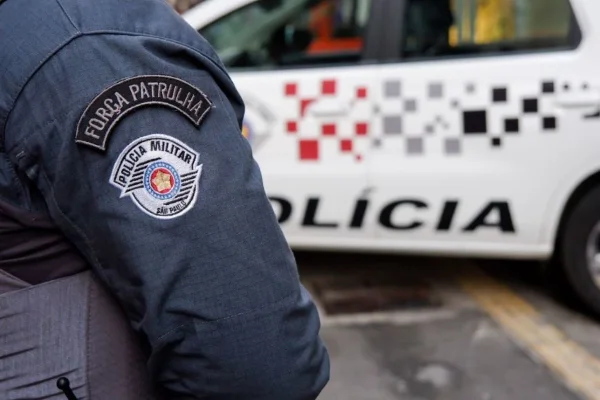 Imagem colorida mostra policial militar e viatura ao fundo. Metrópoles