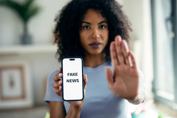 Mulher negra segura um celular com a mão direita. Na mão esquerda, ela tem um celular