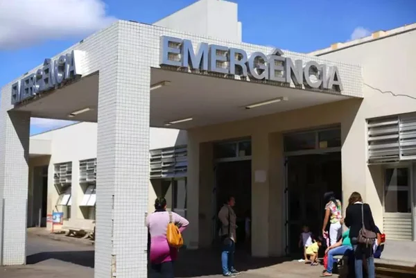 Prédio branco escrito "emergência" e pessoas passando embaixo