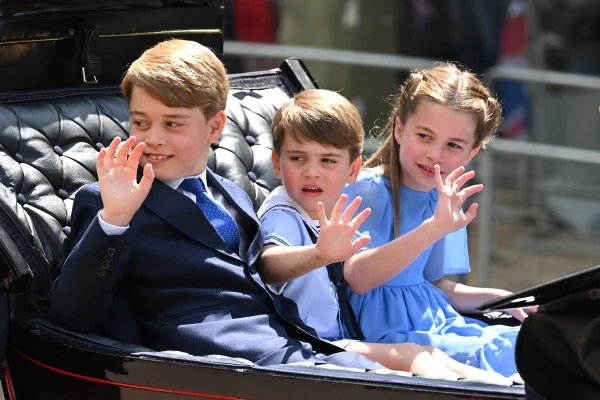 Foto colorida de dois meninos e uma menina em uma carruagem acenando - Metrópoles