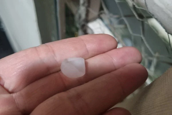 Imagens coloridas mostram pedra de granizo que caiu durante chuva em sacada de apartamento, com rede de proteção ao fundo