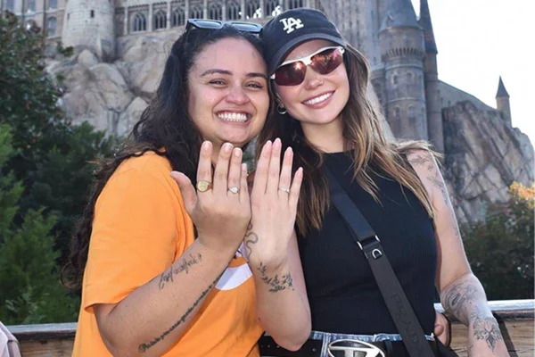 foto colorida de marcella mcgowan de blusa e boné pretos e luiza martins de camiseta laranja mostrando aneis de noivado - metrópoles