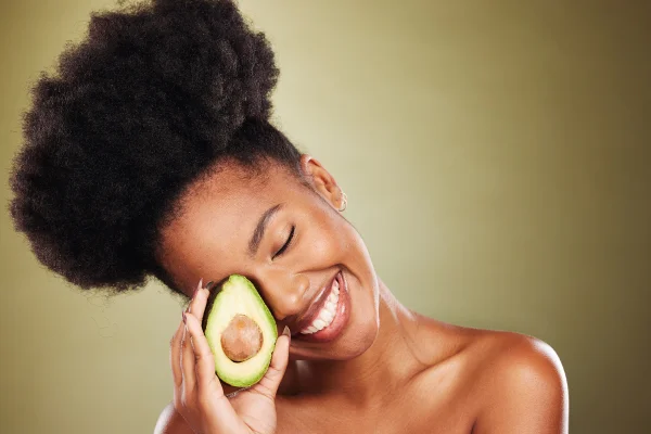 Mulher negra sorrindo se olhos fechados segurando um abacate - Metrópoles