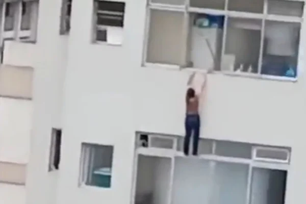 Mulher pendurada em janela de prédio no Guarujá. - Metrópoles