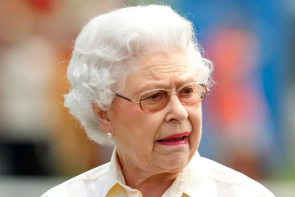 Foto colorida. Rainha Elizabeth faz careta. Ela veste uma blusa branca