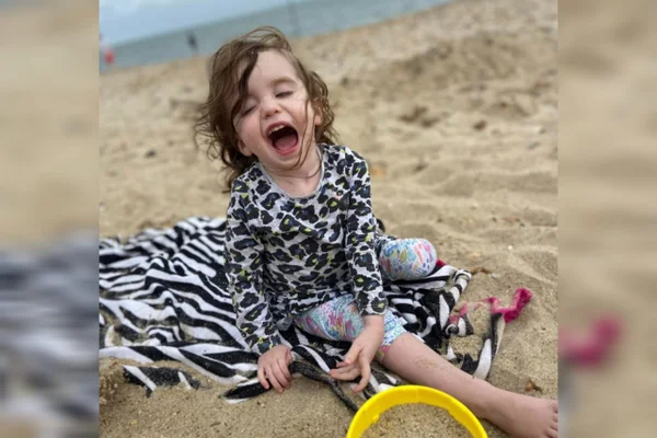 Foto mostra criança brincando em praia. É Imogen, bebê que teve tumor cístico no cérebro - Metrópoles