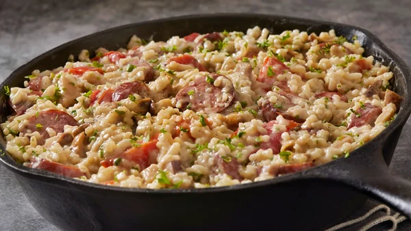 Foto colorida de arroz cremoso com diversos temperos e linguiça calabresa em panela