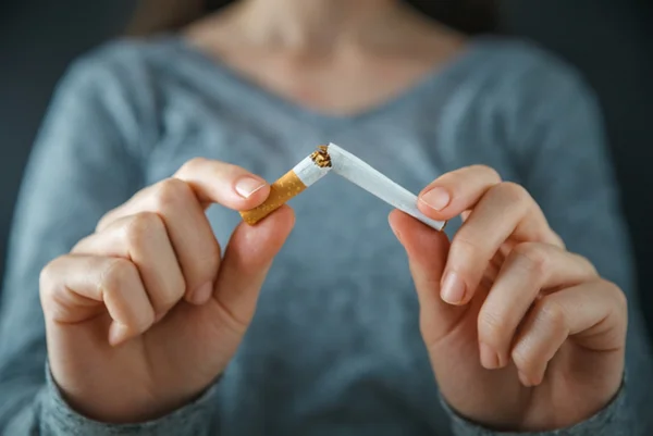 Foto colorida de mulher de suéter quebrando cigarro ao meio - Metrópoles