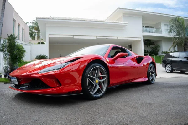 Foto colorida de ferrari vermelha em frente a uma mansão