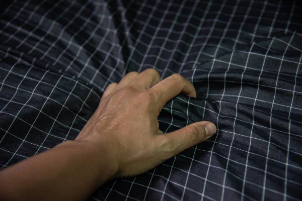 Foto colorida em close de uma mão masculina segurando com força um leçol azul escuro quadriculado - Metrópoles