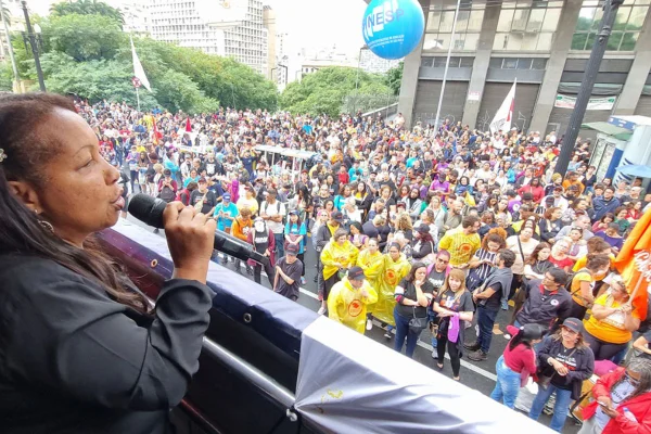 Imagem colorida de assembleia de profissionais da rede municipal de ensino. Foto mostra mulher segurando microfone e multidão ao fundo - Metrópoles