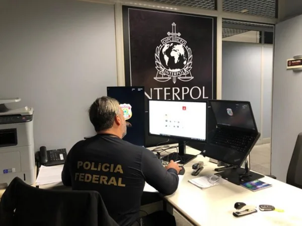 Imagem colorida de agente da PF com símbolo da Interpol atrás