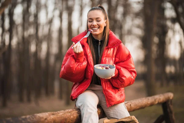 foto colorida de mulher comendo na rua em um dia frio
